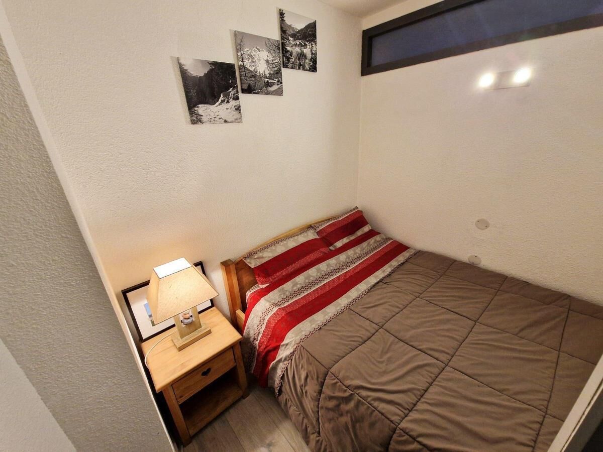 A small, neatly arranged bedroom with a single bed, a bedside table with a lamp, and a window.