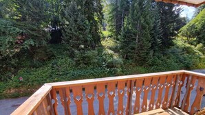A wooden deck with a railing, surrounded by dense greenery and trees.