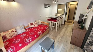 A compact living space with a sofa, a small table, a dining area, and a kitchenette.