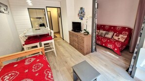 A room with a bed, a small table, a TV, a dresser, and a red sofa.
