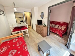 Um quarto com uma cama, uma mesinha, uma televisão, um armário e um sofá vermelho.