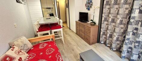 A compact room with a bed, a small table, a TV, and a wardrobe.