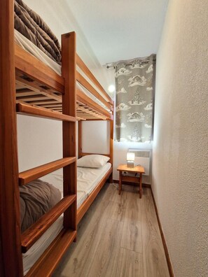 Ein kleiner, kompakter Raum mit einem Etagenbett, einem Nachttisch mit Lampe und einem Fenster mit Vorhang.