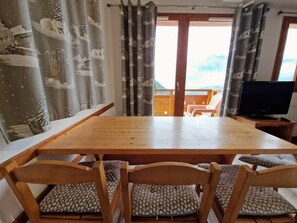 Ein Holzespeisesaal mit vier Stühlen, einem Fernseher auf einem Schrank und Blick auf Berge durch eine Glastür.