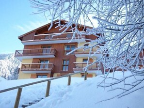 Ein mehrstöckiges Holzhaus mit Balkonen, umgeben von schneebedeckten Bäumen und Bergen.