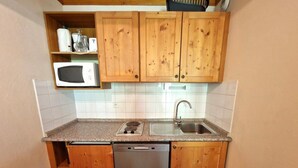 Kompakti keittiö, jossa on puukalusteet, mikroaaltouuni, astianpesukone ja pesuallas.