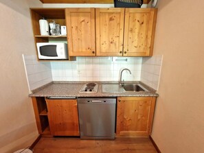 Cozinha compacta com armários de madeira, micro-ondas, lava-louças e pia.