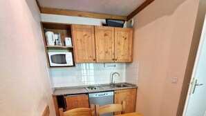 Kompakti keittiö, jossa on puiset kaapit, mikroaaltouuni, pesuallas ja ruokapöytä tuoleineen.
