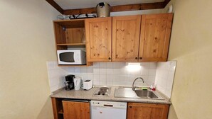 Cozinha compacta com armários de madeira, micro-ondas, lava-louças e pia.