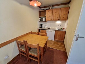 A compact kitchen with wooden cabinets, a microwave, a dishwasher, and a dining table with chairs. - 100m from resort center, 1st floor, view mountain, terrace, balcony, tv, ski locker, 28m², Valfréjus (Valfréjus)