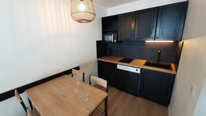 A compact kitchen with dark cabinets, a microwave, a dishwasher, and a wooden dining table with two chairs.