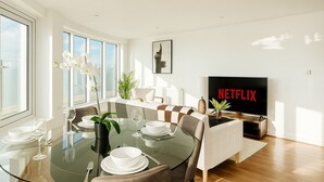 A modern dining area with a glass table, white plates, and a Netflix TV. - Luxury Penthouse in Harrow | 2BR | Gym | Games | Lounge | Free Parking (Harrow)