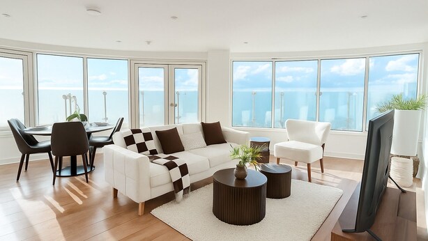 A modern living room with a white sofa, black and white checkered throw, a round coffee table, and a TV stand. Large windows offer a view of the ocean. - Luxury Penthouse in Harrow | 2BR | Gym | Games | Lounge | Free Parking (Harrow)