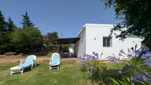 A white house with a patio area, two lounge chairs, and a barbecue setup.