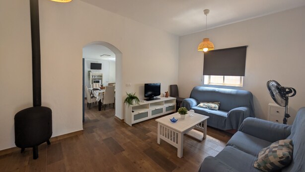 A modern living room with a sofa, TV, and a dining area visible through an archway.