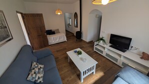 A modern living room with a blue sofa, a white coffee table, a TV on a white stand, and a hanging light fixture.