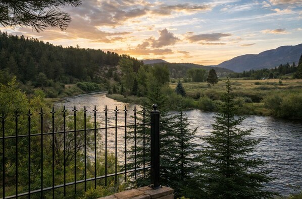 A river with a metal fence, surrounded by trees and hills.