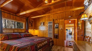L’intérieur d’une cabane en bois comprend un grand lit, une table à manger et un couloir qui mène à une autre pièce.