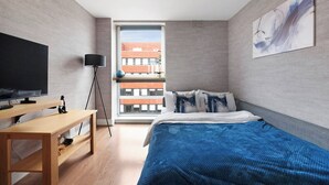 Quarto moderno com cama grande, televisão, escrivaninha e vista para um prédio através de uma janela.