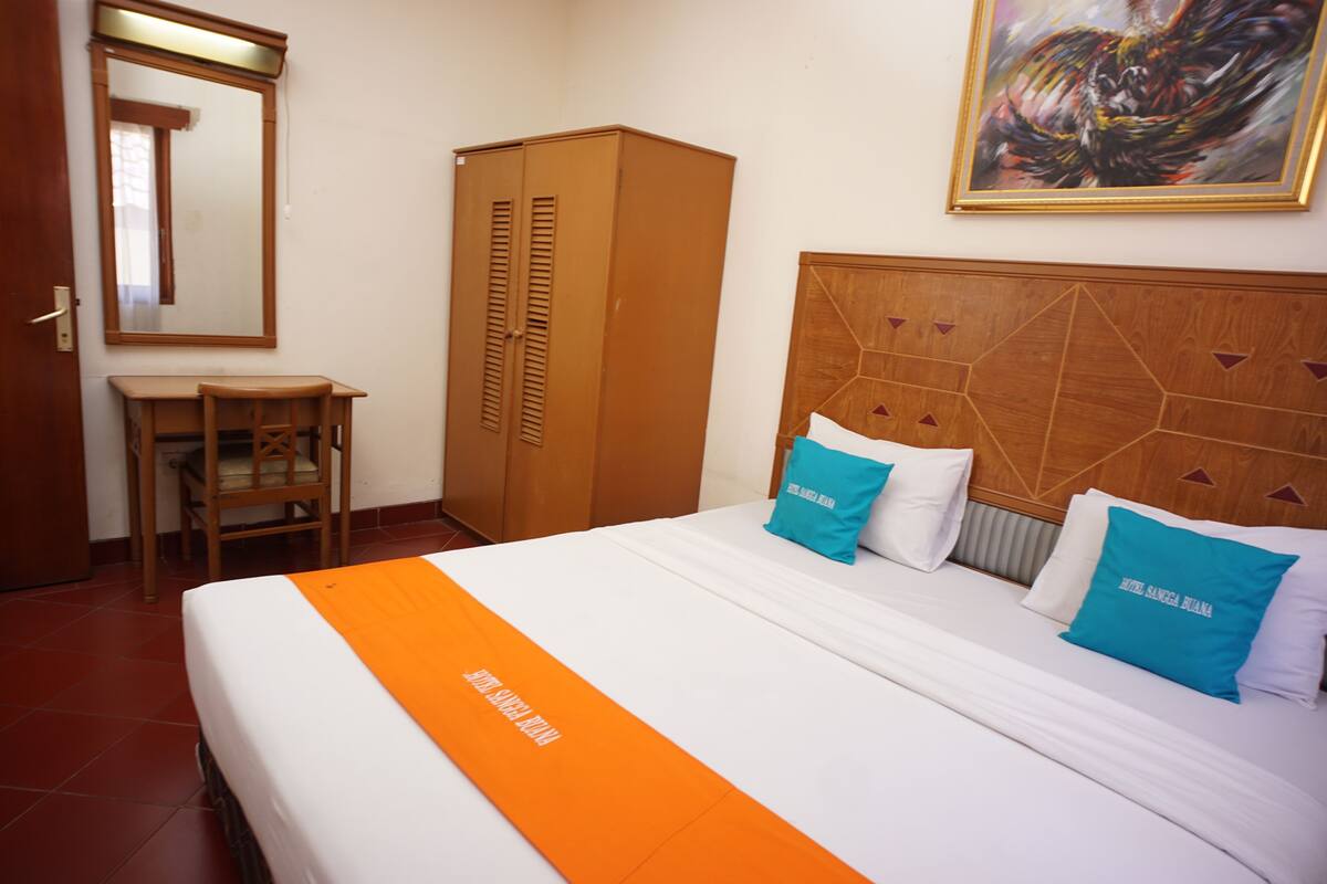 Habitación de hotel con cama, escritorio, silla, armario y un cuadro en la pared.