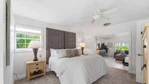 Une chambre avec un grand lit, deux tables de chevet avec des lampes, un ventilateur de plafond et une vue sur un balcon.