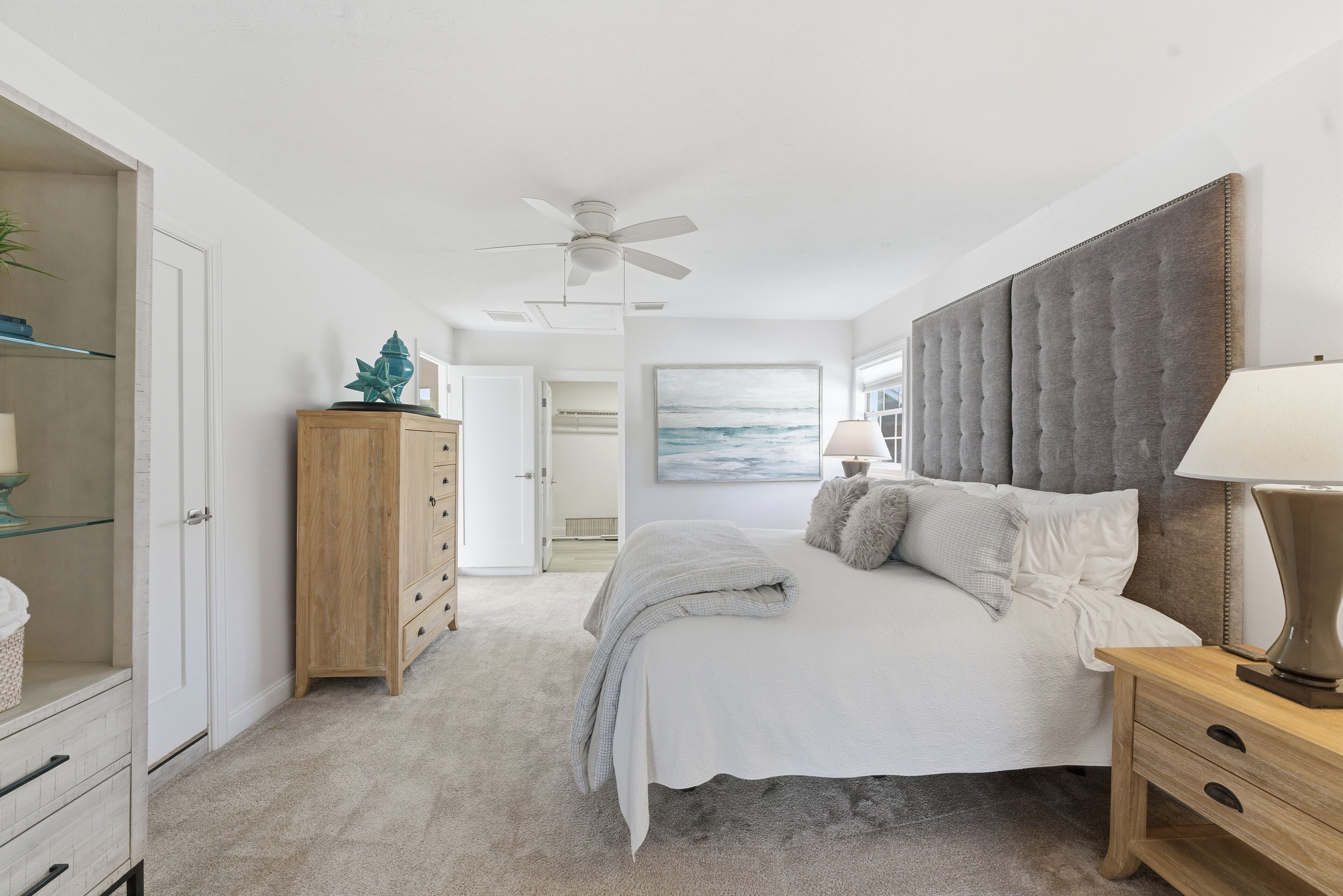 A bedroom with a bed, a nightstand, a ceiling fan, a wardrobe, and a painting on the wall.