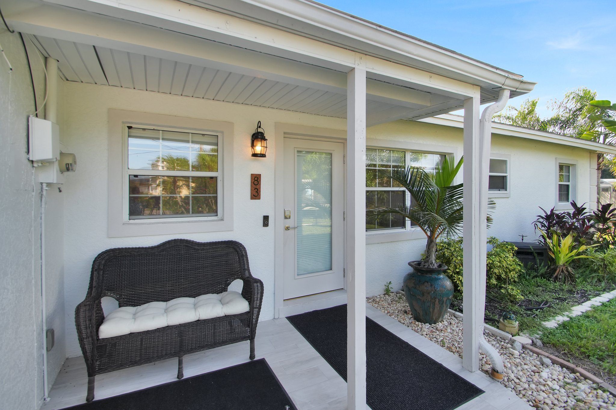 A house with a porch, a bench, a potted plant, and a door with a number.