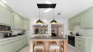 Une cuisine spacieuse avec des meubles de couleur verte, un îlot central doté de tabourets et un éclairage suspendu.