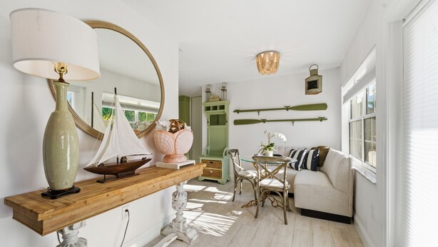 Une pièce lumineuse avec une console en bois, un vase vert, une maquette de voilier, un meuble vert, un canapé blanc et une lanterne suspendue.