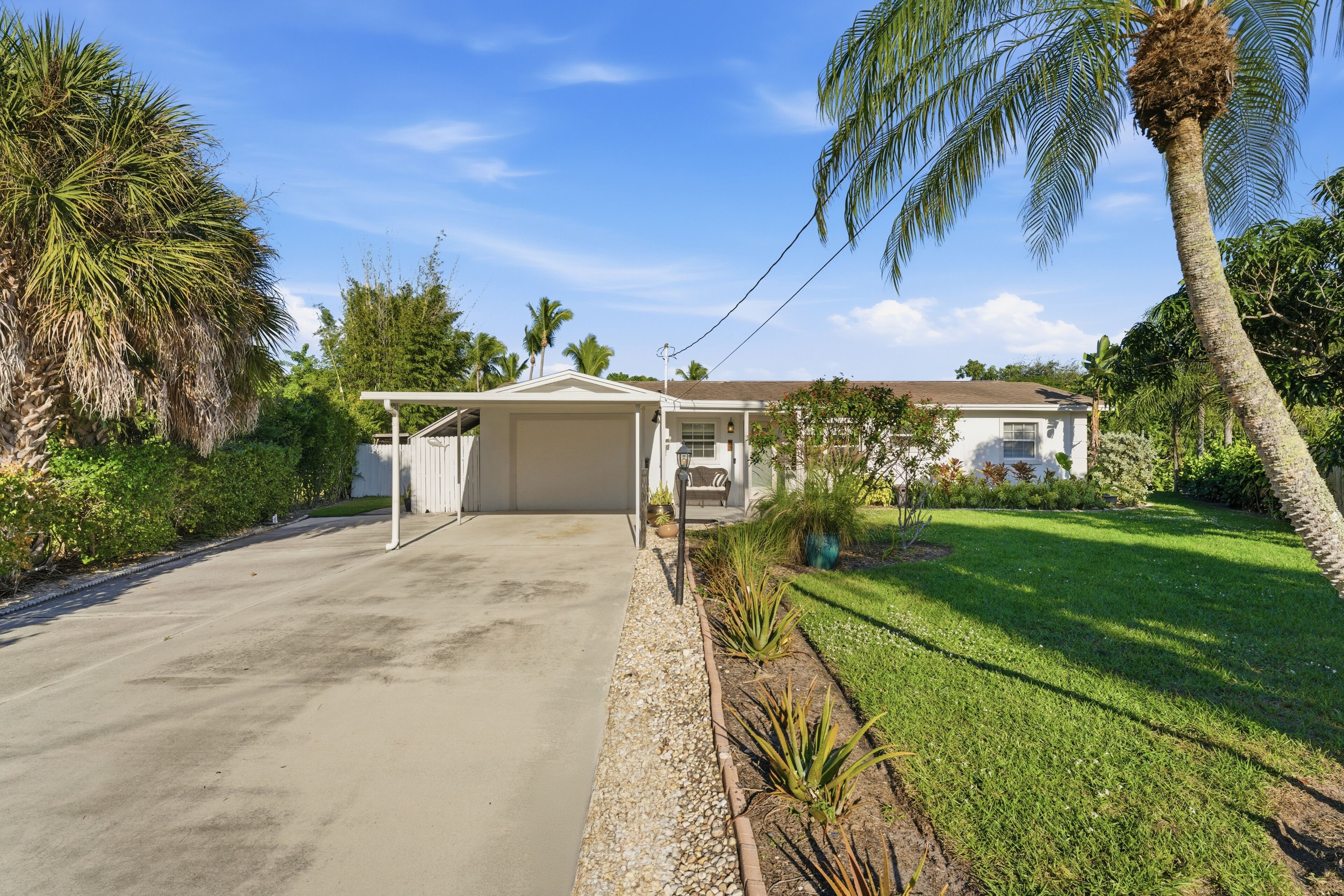 A single-story house with a covered garage, surrounded by a well-maintained lawn and palm trees.