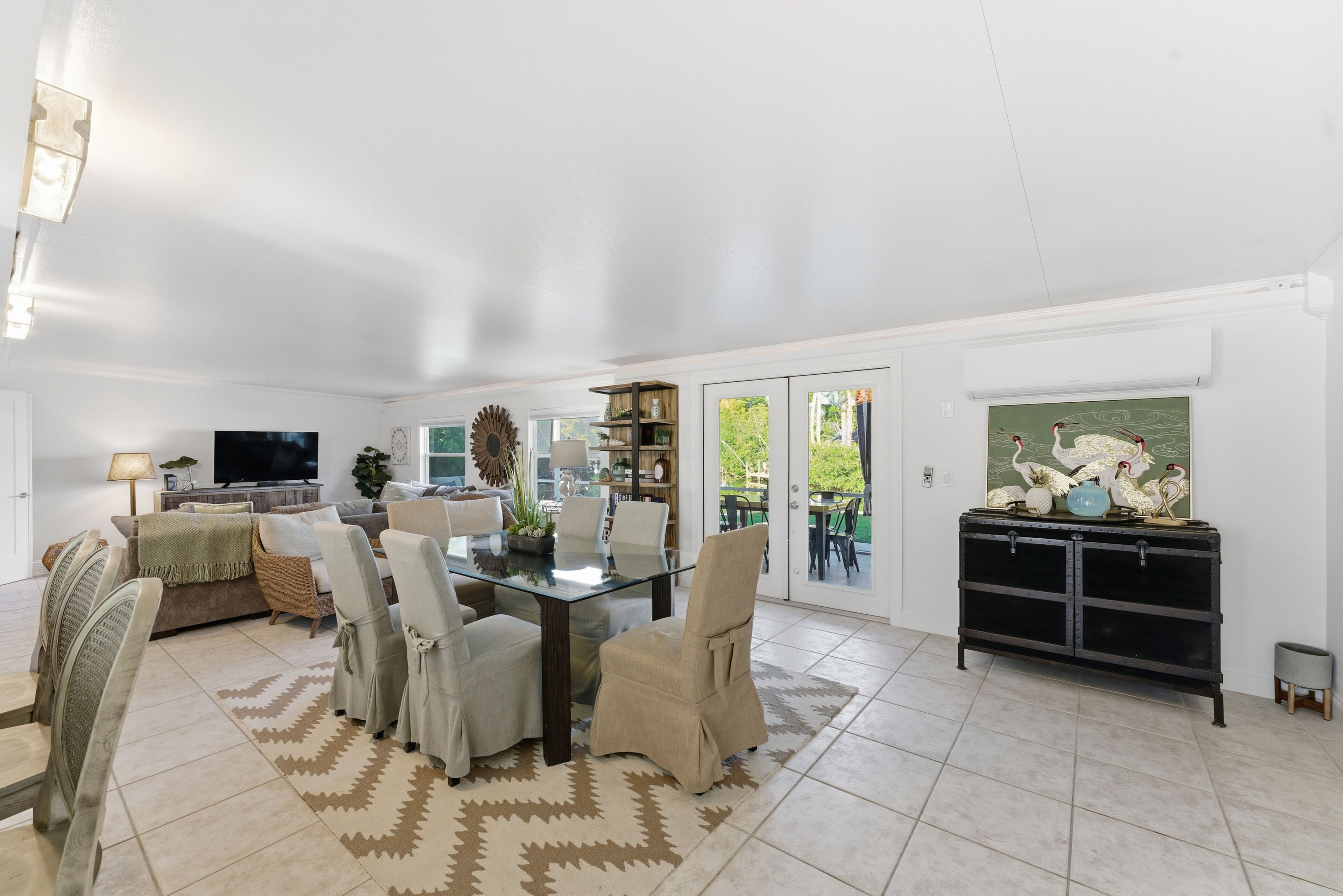 A spacious living room with a glass-top dining table, comfortable seating, a television, and a view of the outdoors.