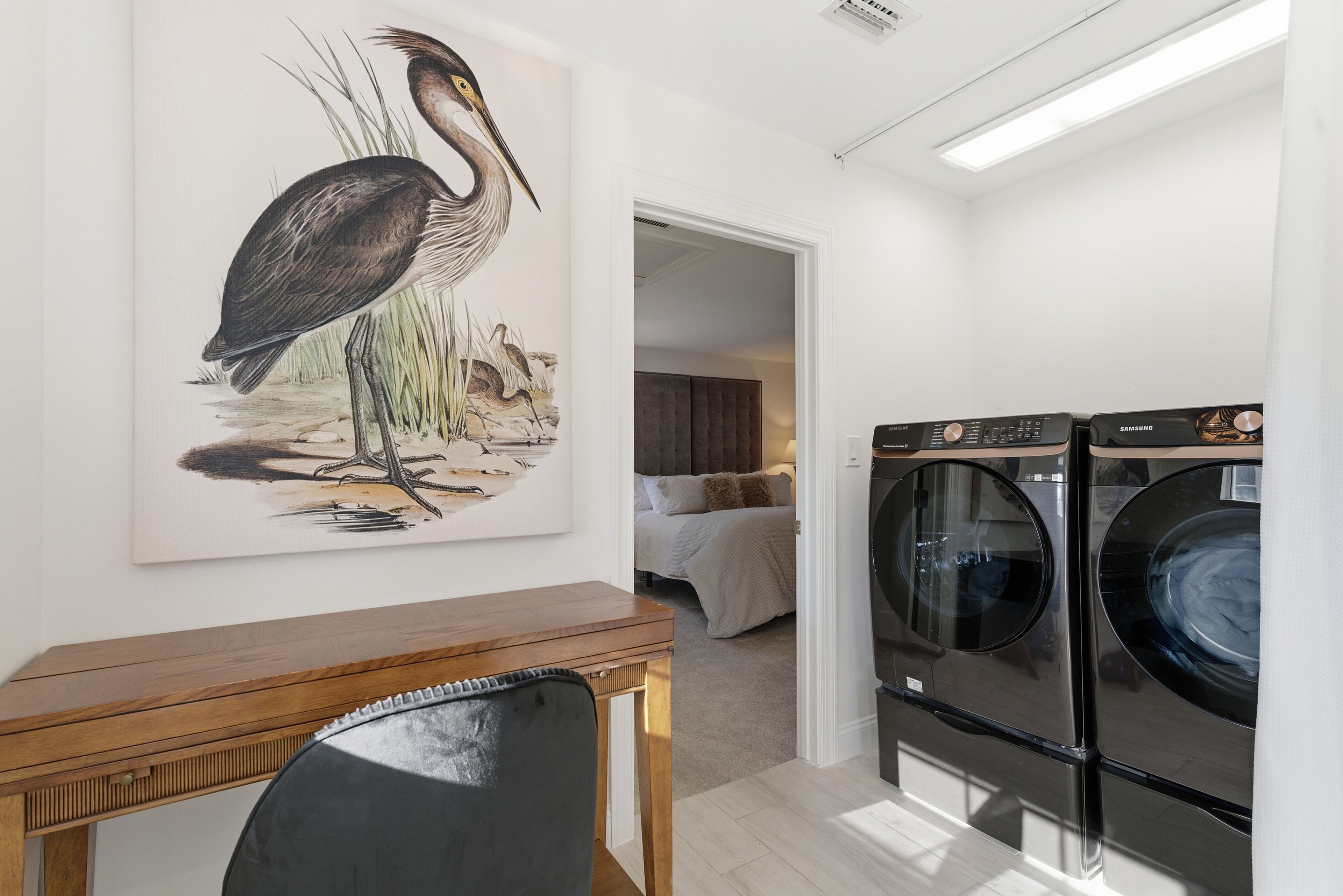 Une buanderie avec deux machines à laver noires, une table en bois et une grande peinture murale représentant un oiseau et des roseaux.