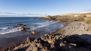 A rocky beach with a lighthouse, a small building, and people sunbathing. - TenoHomes Elegant Hideaway in Nature (Puertito de los Silos)
