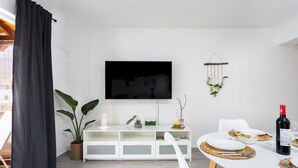 A modern living room with a white sofa, a dining table set for two, a flat-screen TV, and a potted plant. - TenoHomes Elegant Hideaway in Nature (Puertito de los Silos)