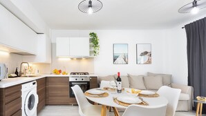 A modern kitchen with a built-in washing machine, a dining area with a round table and white chairs, and a living area with a sofa and a TV. - TenoHomes Elegant Hideaway in Nature (Puertito de los Silos)
