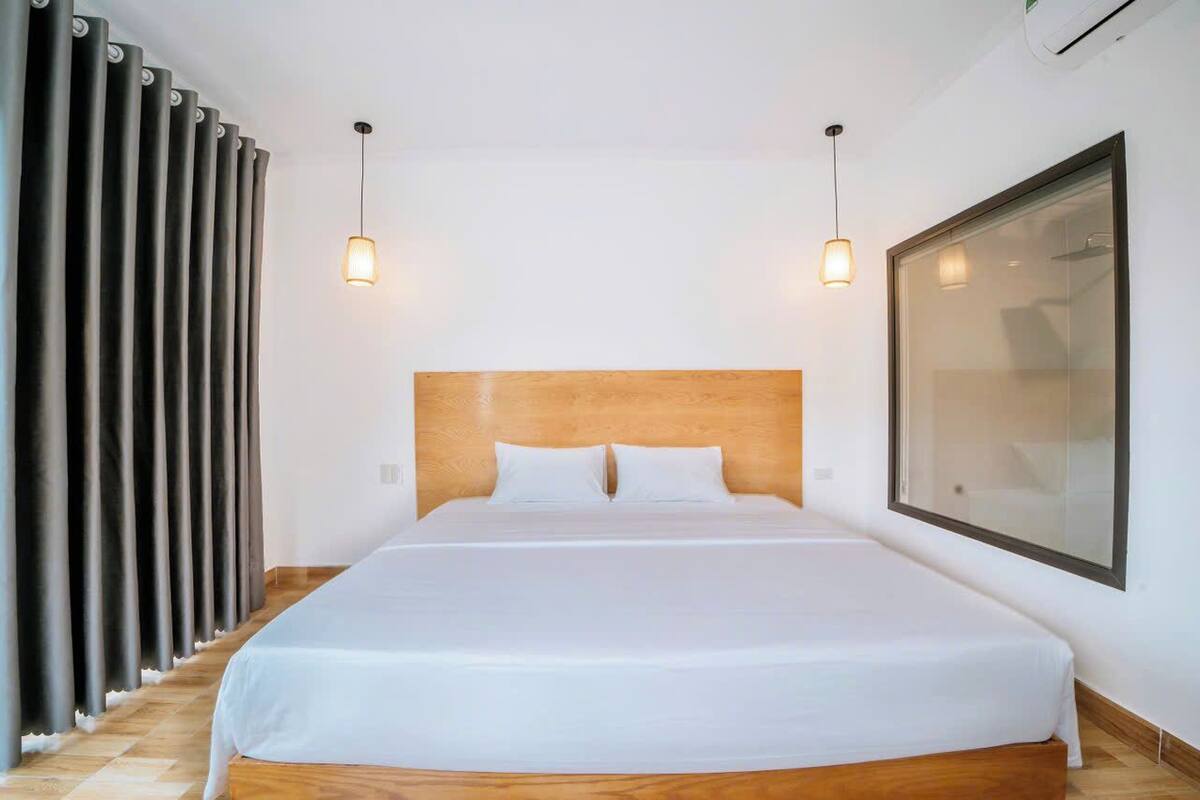 Una habitación de hotel moderna con una cama grande, cabecero de madera y un ventanal amplio.