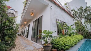 Ein modernes Haus mit überdachter Terrasse, Swimmingpool und verschiedenen Pflanzen.