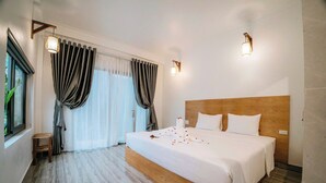 Ein Hotelzimmer mit einem großen Bett, einem Holzkopfende, zwei Wandleuchten, einem Fenster mit Vorhängen und einem kleinen Holzschemel.