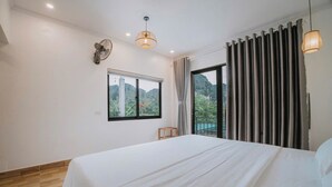 Ein Schlafzimmer mit einem großen Bett, einem Fenster mit Blick auf Grünflächen, einem Deckenventilator und einer Hängeleuchte.