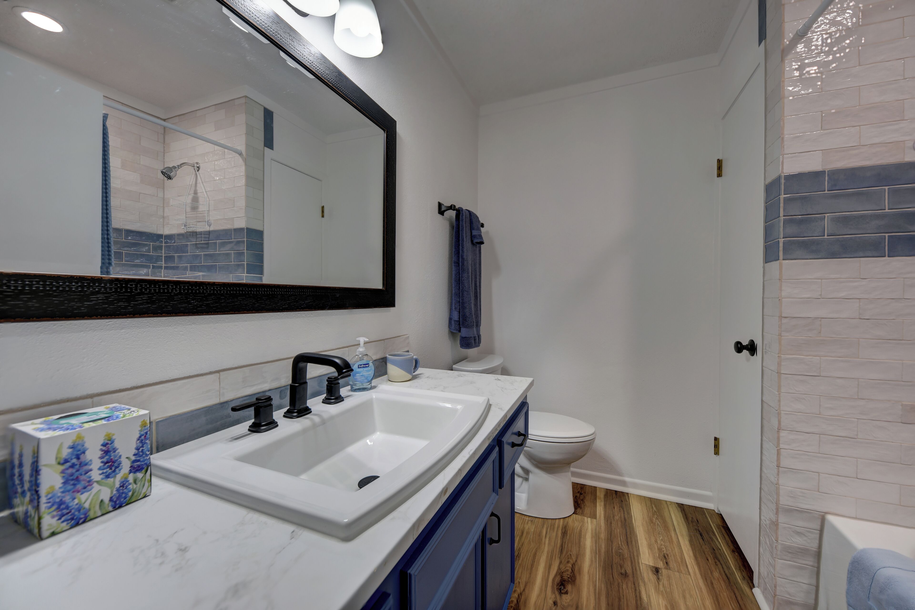 A bathroom with a white sink, black faucet, and a mirror above it. There is a blue towel hanging on a hook and a toilet next to the mirror.