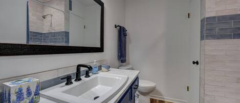 A bathroom with a white sink, black faucet, and a mirror above it. There is a blue towel hanging on a hook and a toilet next to the mirror.