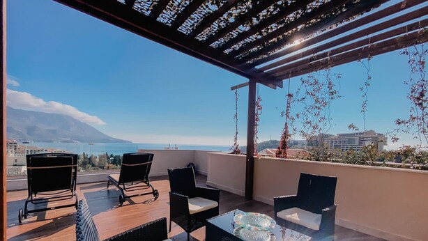 Un balcon avec vue sur la mer et les montagnes, aménagé avec des chaises et une table.