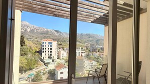 Un balcon agrémenté d’une pergola, d’une chaise et offrant une vue sur un paysage montagneux parsemé de bâtiments.