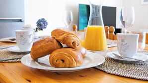 Une table en bois dressée pour le petit-déjeuner, avec des croissants, un verre de jus d’orange et une tasse de café.