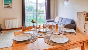 Un coin repas avec une table en bois dressée pour quatre personnes, un canapé et une vue sur l’extérieur.