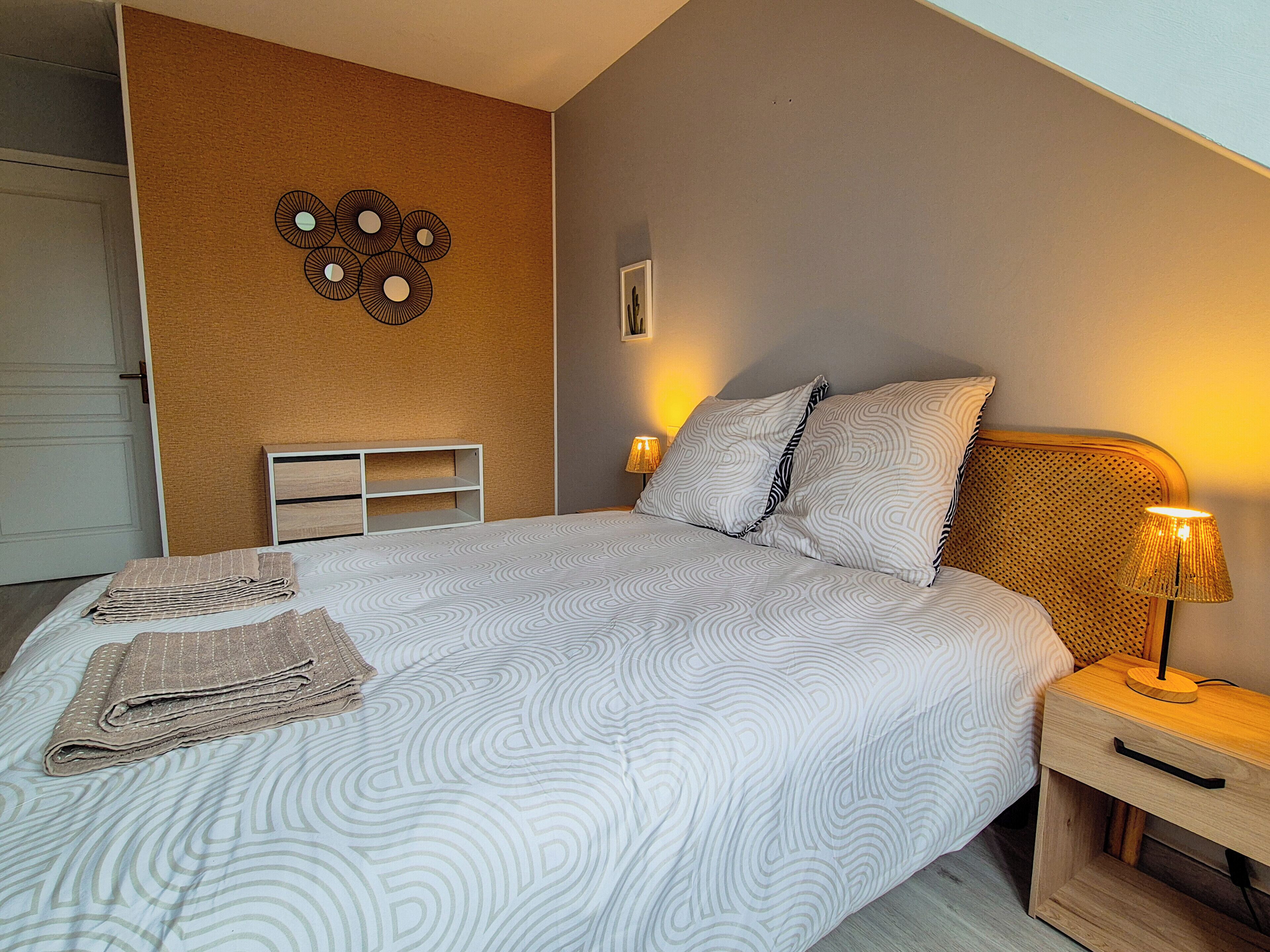Un lit bien fait, avec une literie à motifs, une table de chevet avec une lampe et un élément décoratif fixé au mur.