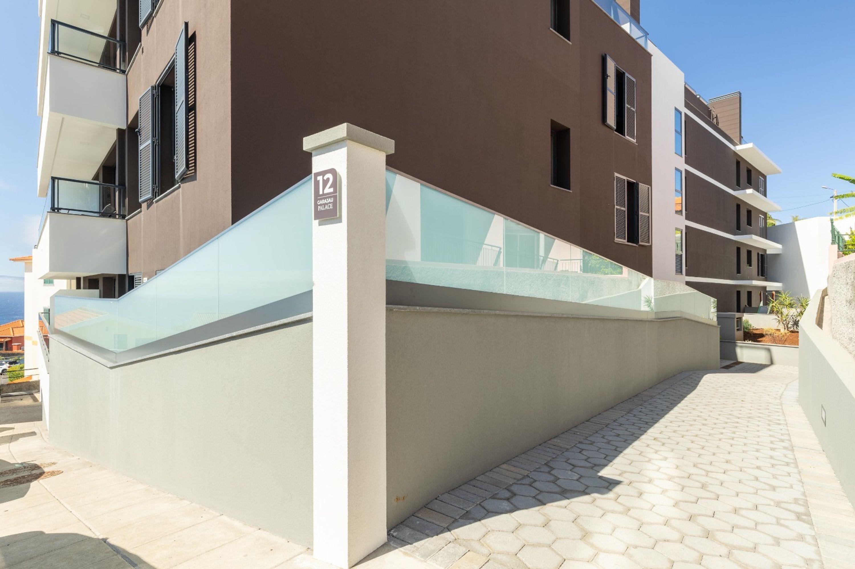 Un bâtiment moderne doté d’un balcon en verre, d’une enseigne indiquant qu’il s’agit du « 12, place Girasu », et d’un trottoir dallé.