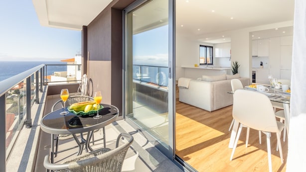 A modern apartment with a balcony overlooking the sea, a dining area with a table set for two, and a living room with a sofa and a dining table. - Garajau Sea Side by Atlantic Holiday (Santa Cruz)