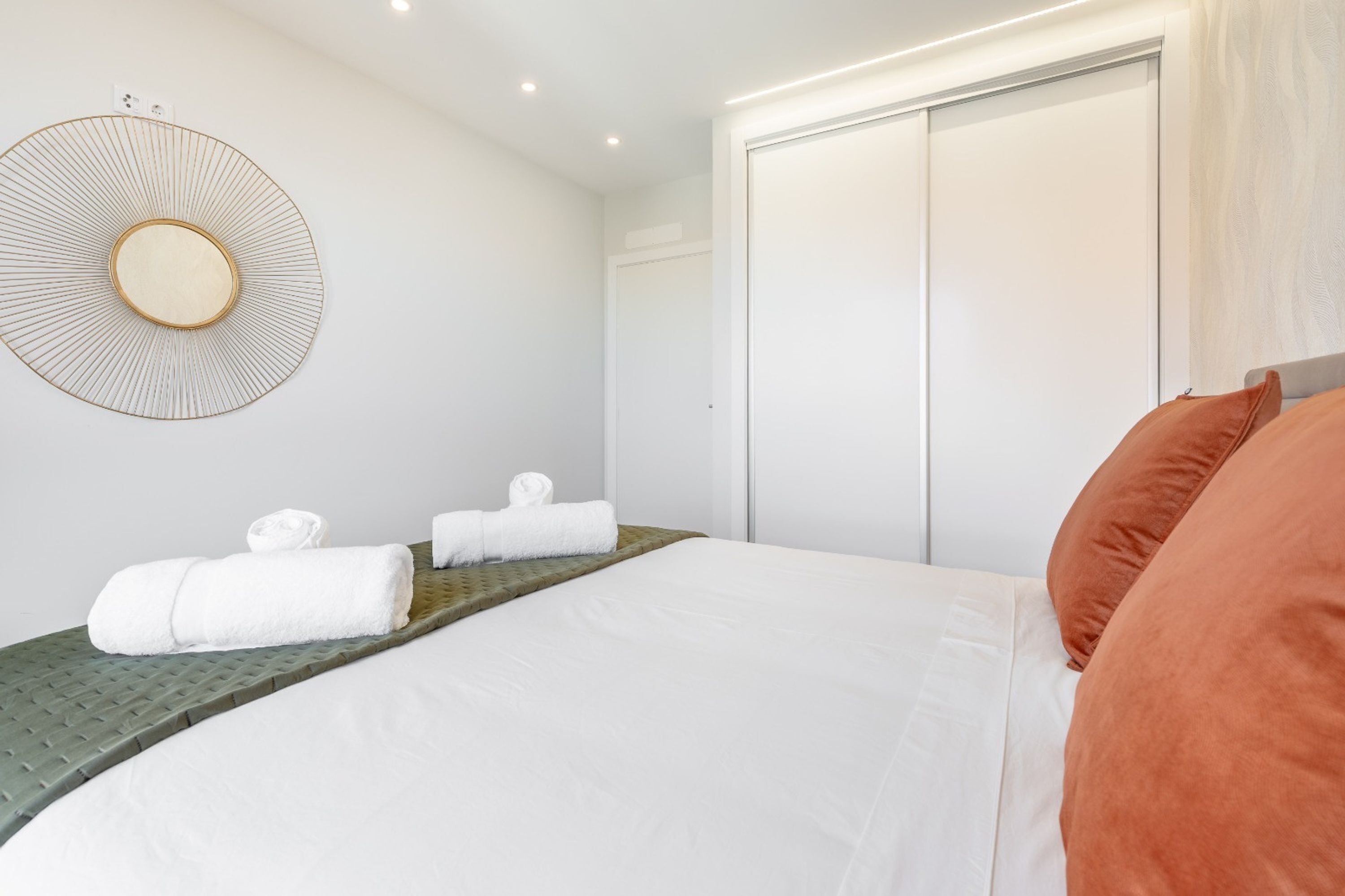 A modern hotel room with a large bed, a round mirror, and a wardrobe.