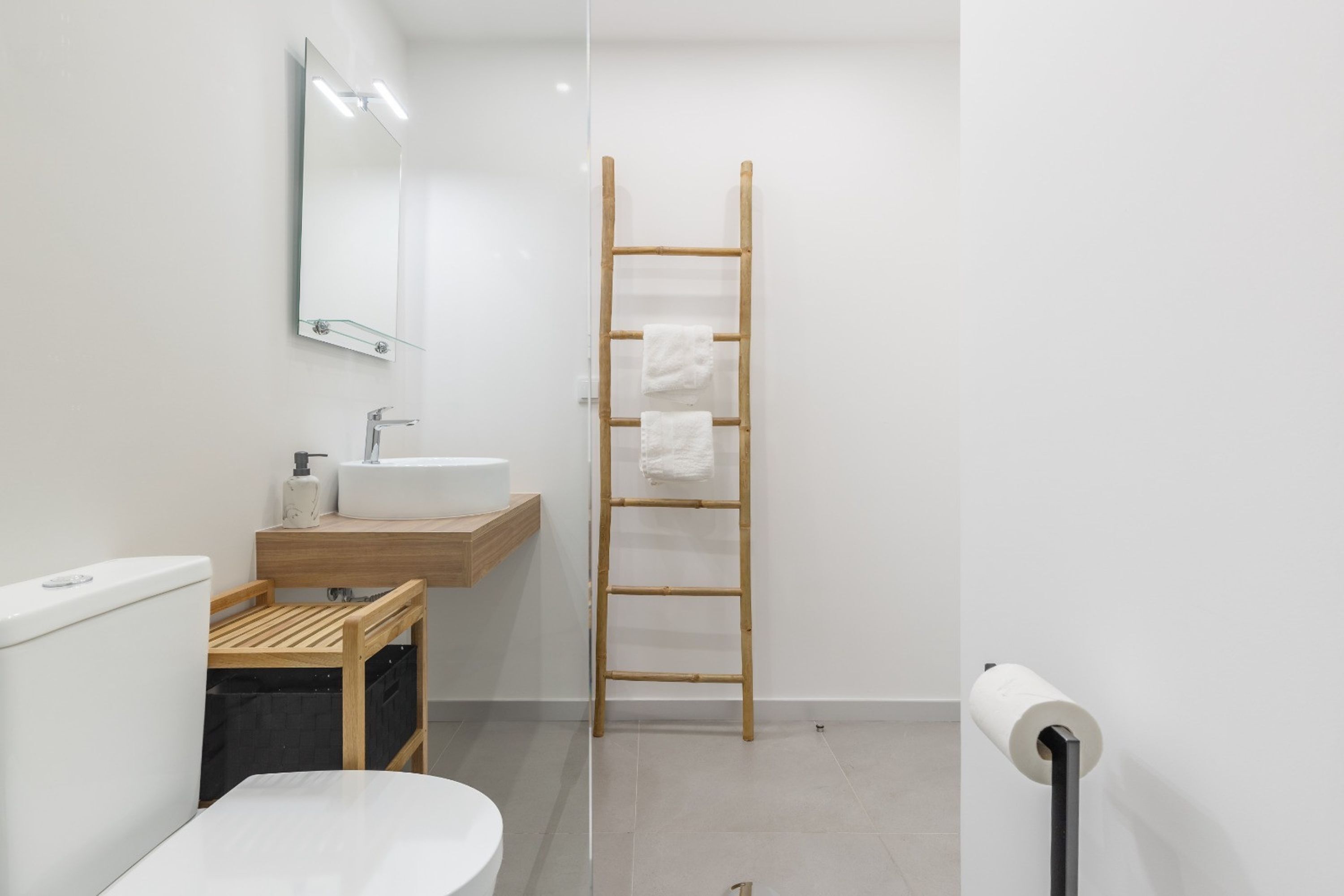 Un bagno moderno con lavandino, specchio e water bianchi. Una scala in legno con un asciugamano appeso.